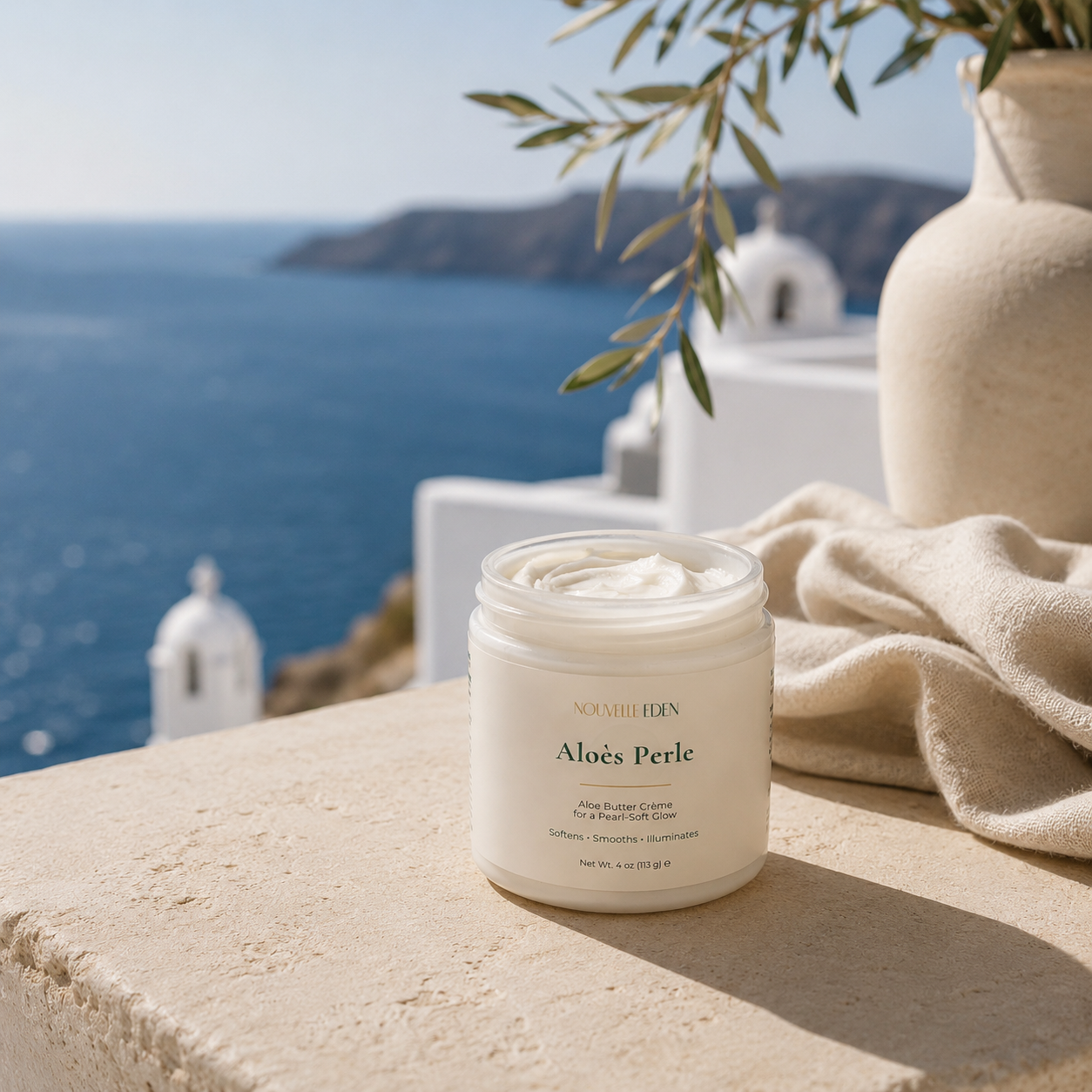 Jar of Aloe Perle cream on a ledge with a scenic ocean view and white buildings.